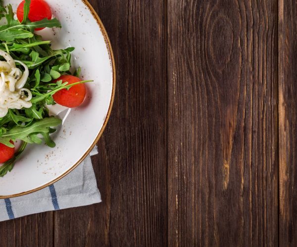 A delightful arugula salad with tomatoes and cheese, served on a rustic wooden table, perfect for healthy eating.